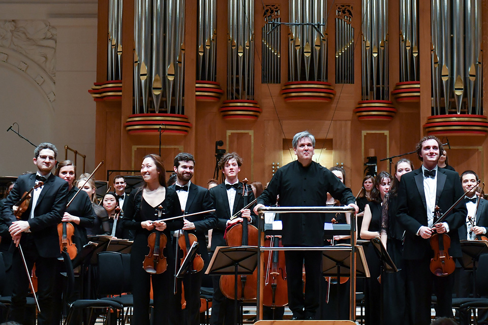 Sir Antonio Pappano smiling facing the audience with the students in the orchestra in the RCM's Amaryllis Fleming Concert Hall